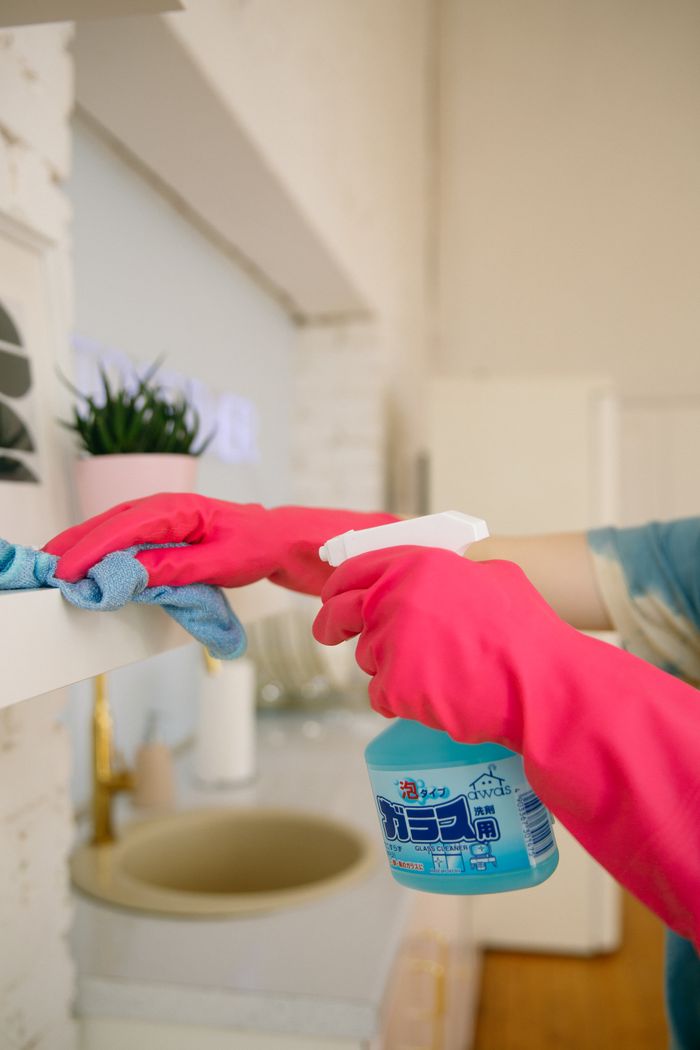 A person cleans a kitchen shelf with a spray bottle and cloth, keeping the space hygienic and clean.